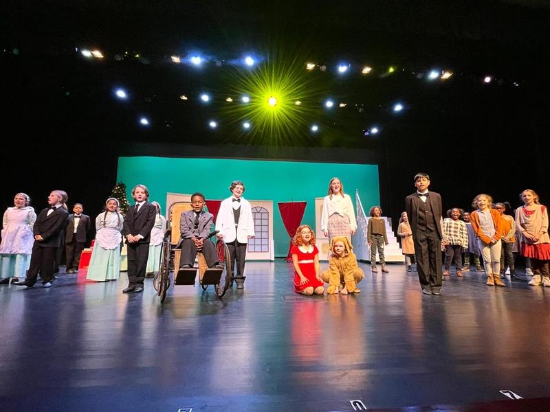 A group of students stand on stage in costume for Annie Jr. during the final number